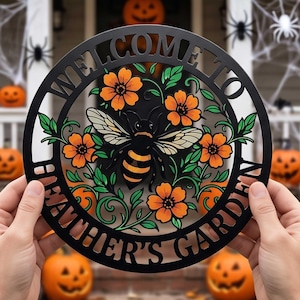 May include: A circular black metal sign featuring the text "WELCOME TO HEATHER'S GARDEN" cut out along the border. The center displays a detailed illustration of a bee surrounded by orange flowers and green leaves, crafted with a cutout design.