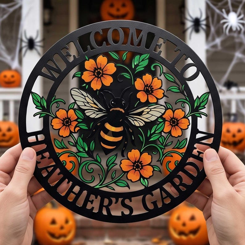 May include: A circular black metal sign featuring the text "WELCOME TO HEATHER'S GARDEN" cut out along the border. The center displays a detailed illustration of a bee surrounded by orange flowers and green leaves, crafted with a cutout design.