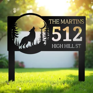 Pode incluir: Placa de endereço de metal preto com uma silhueta de lobo uivando contra uma lua e uma floresta. A placa exibe "THE MARTINS" acima dos números "512" e "HIGH HILL ST". A placa é montada em dois postes pretos.