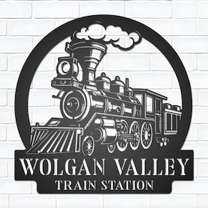 Könnte beinhalten: Schwarze Metall-Wandkunst mit einer detaillierten Zugsilhouette mit Rauch. Der Text "WOLGAN VALLEY TRAIN STATION" wird unter dem Zug in einem dekorativen Rahmen angezeigt. Das Kunstwerk ist an einer weißen Backsteinmauer befestigt.