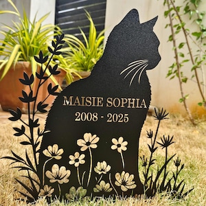 Könnte beinhalten: Schwarzes Metall-Garten-Denkmal in Katzenform mit dem Namen "Maisie Sophia" und den Daten "2008 - 2025" in Gold geätzt. Die Katze ist von stilisierten Blumen und Blättern umgeben, geeignet für den Außenbereich.