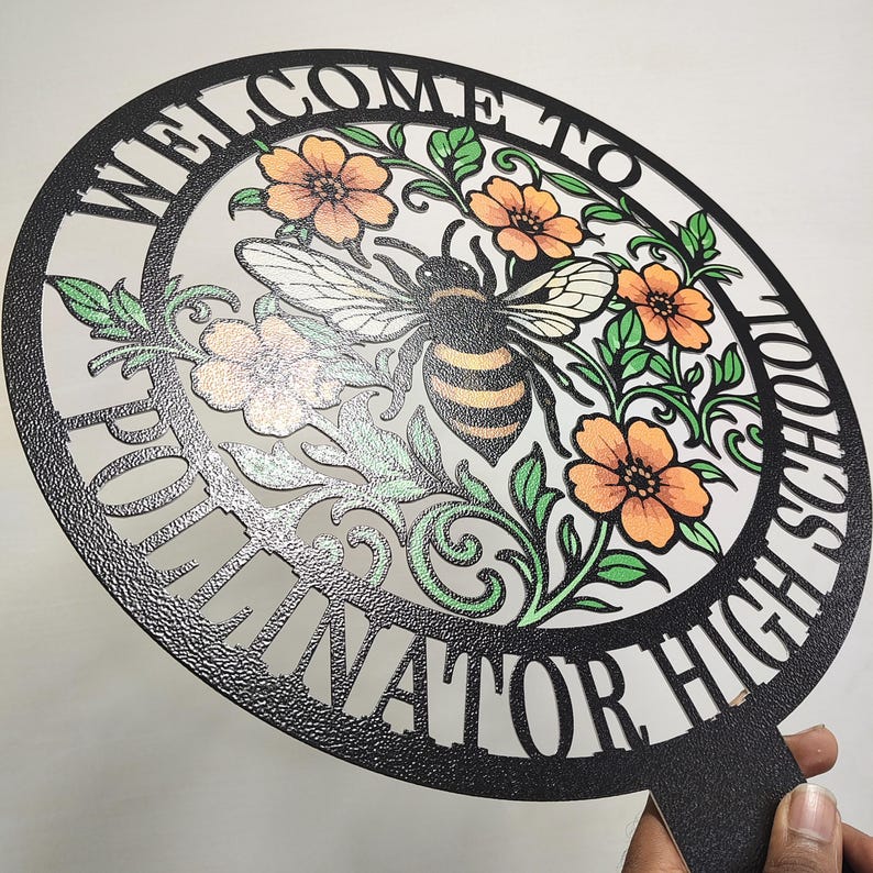 May include: A circular black sign with a textured finish featuring the text "WELCOME TO POLLINATOR HIGH SCHOOL" cut out along the border. The center displays a detailed illustration of a bee surrounded by orange flowers and green leaves.