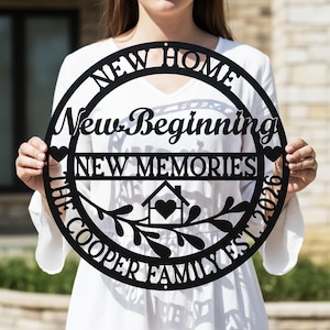 May include: Black metal sign with the words "NEW HOME, New Beginning, NEW MEMORIES, THE COOPER FAMILY EST. 2026". The sign has a house with a heart inside and decorative leaves.