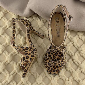 K&ouml;nnte beinhalten: Ein Paar High-Heel-Sandalen mit Leopardenmuster. Die Sandalen haben einen d&uuml;nnen Kn&ouml;chelriemen und einen Riemen &uuml;ber den Zehen. Der Markenname "GELTONY" ist auf der Innensohle sichtbar. Die Abs&auml;tze sind etwa 10 cm hoch.