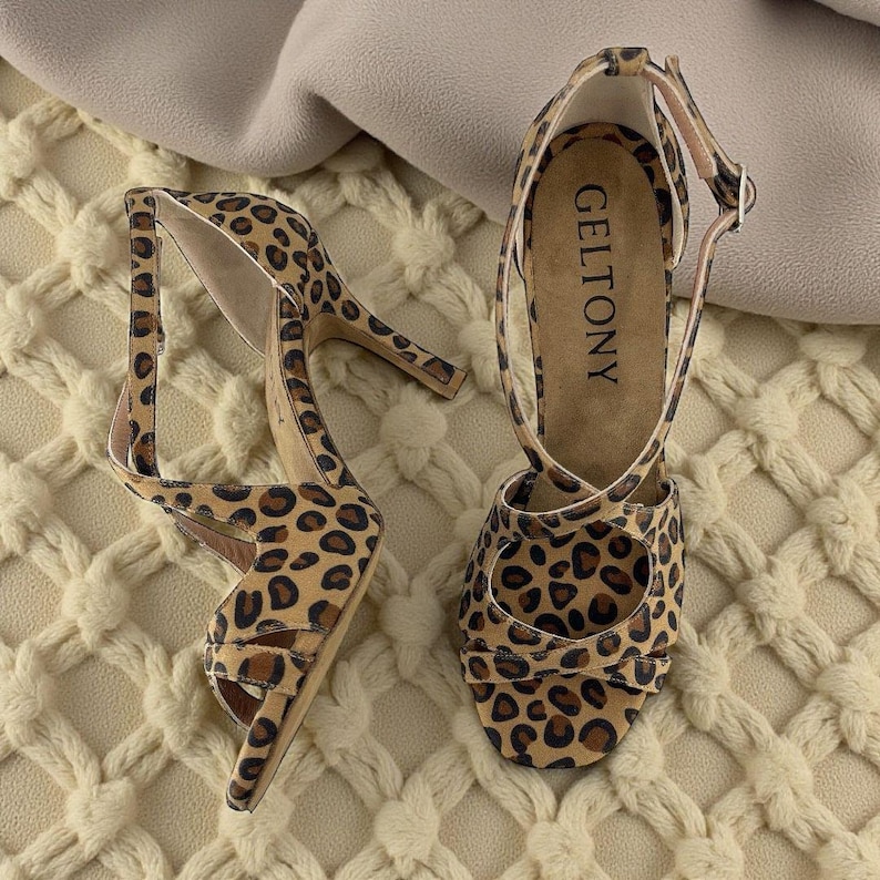 K&ouml;nnte beinhalten: Ein Paar High-Heel-Sandalen mit Leopardenmuster. Die Sandalen haben einen d&uuml;nnen Kn&ouml;chelriemen und einen Riemen &uuml;ber den Zehen. Der Markenname "GELTONY" ist auf der Innensohle sichtbar. Die Abs&auml;tze sind etwa 10 cm hoch.