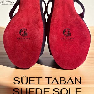 K&ouml;nnte beinhalten: Nahaufnahme von schwarzen High Heels mit leuchtend roten Wildledersohlen. Die Sohlen zeigen das "GELTONY"-Logo. Der Text "SUEDE SOLE" ist unten im Bild zu sehen.