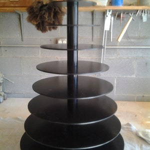 May include: A black, tiered, rotating display stand with seven circular shelves. The stand is made of wood and has a black finish.