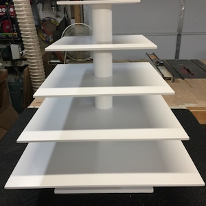 May include: A white five-tier cake stand with square tiers. The stand is made of wood and has a white painted finish.