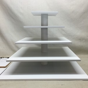 May include: White tiered cake stand with five levels. The stand is made of wood and has a simple, modern design.