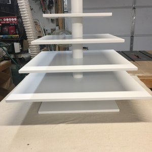 May include: A white four-tiered cake stand with square shelves. The stand is made of wood and has a simple, modern design.