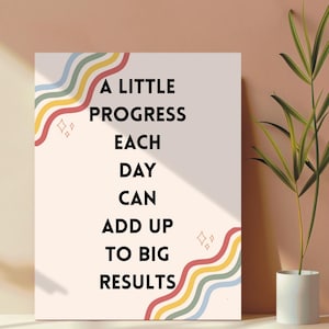 May include: A motivational art print with the text "A Little Progress Each Day Can Add Up To Big Results." The print features colorful wavy lines and diamond shapes on a cream background. A plant in a white pot is in the background.