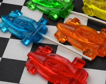 May include: Five translucent hard candy lollipops shaped like race cars in red, orange, yellow, green, and blue. Each candy is attached to a thin white paper stick. The lollipops feature molded details representing the car body, wheels, and cockpit.