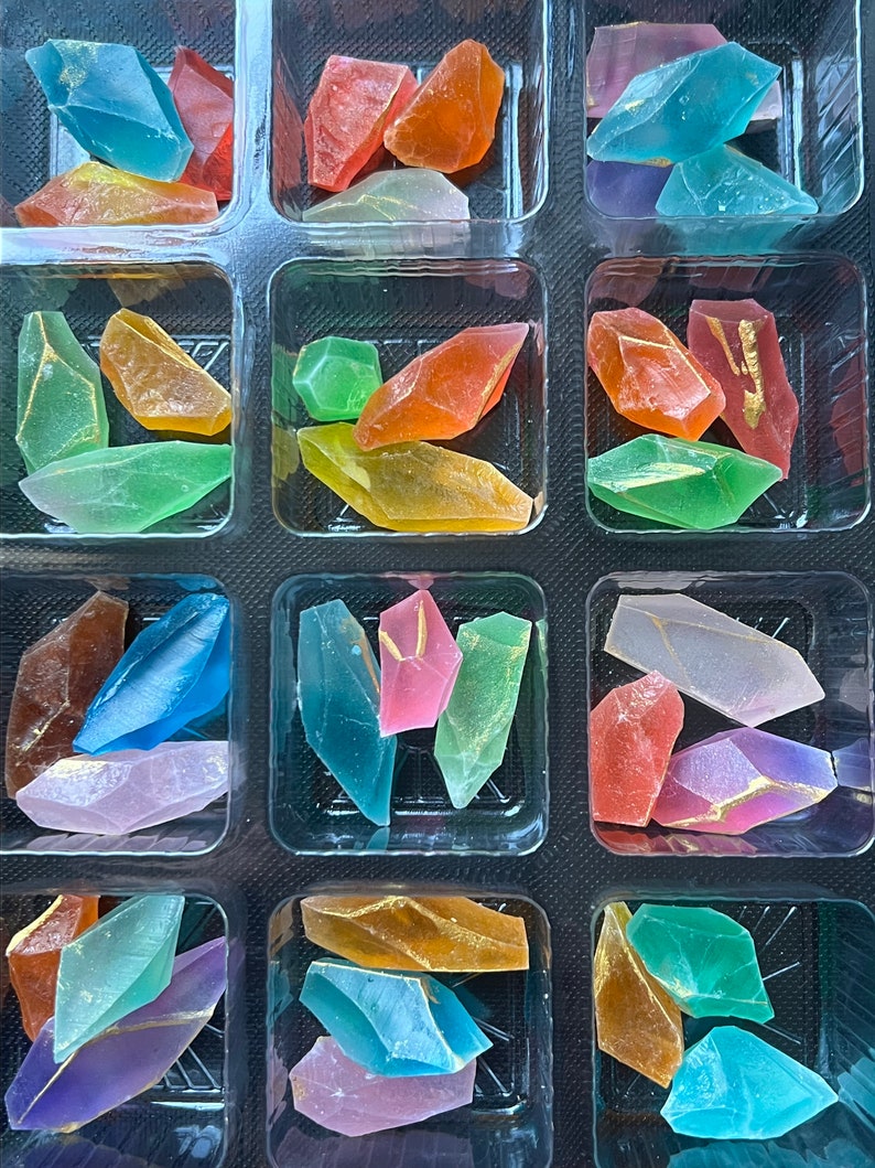 May include: A clear plastic container filled with colorful, translucent, irregularly shaped candy pieces. The candy is arranged in rows and columns, with each compartment containing a different color.