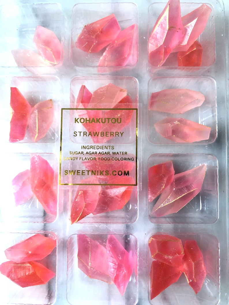 May include: A clear plastic container filled with pink strawberry flavored Kohakutou candy. The candy is shaped like small, irregular crystals. The label on the container reads "Kohakutou Strawberry" and lists the ingredients: sugar, agar agar, water, candy flavor, and food coloring. The website address "sweetniks.com" is printed on the label.