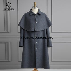 Może przedstawiać: Szary wełniany płaszcz z peleryną i trzema białymi guzikami. Płaszcz ma długie rękawy i kołnierz. Na płaszczu wydrukowano słowa "HISTORICAL COSTUME ERA". Płaszcz jest prezentowany na manekinie.