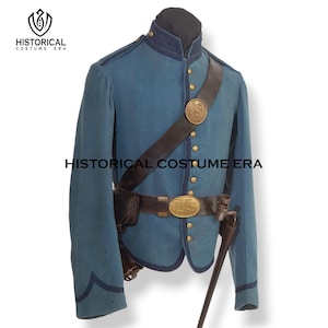 May include: A blue military-style jacket with dark blue trim, featuring a high collar, brass buttons, and a black leather belt with a brass buckle marked US. A diagonal leather strap with a circular brass emblem crosses the chest of the jacket.