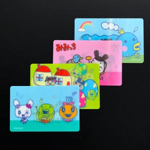 May include: Four colorful rectangular cards with cartoon characters and Japanese text. The cards feature various designs, including houses, musical notes, and a rainbow. The cards are in shades of blue, pink, and green.