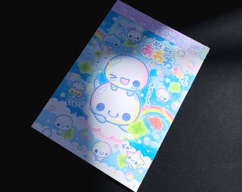 Könnte beinhalten: Ein rechteckiger Notizblock mit einem holografischen oberen Streifen, der einen blauen Hintergrund mit bunten Cartoon-Blasen, Sternen, Regenbögen und lächelnden Charakteren zeigt. Der japanische Text lautet "Puku Puku Awa Awa Chan" mit Phrasen wie "Moko Moko" und "Yoroshiku".