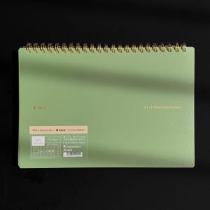 May include: A5 size spiral-bound notebook with a light green cover. The notebook features gold lettering and a gold spiral binding. Text on the cover includes "kleid", "Mnemosyne", and "702 | Mnemosyne". The notebook contains 70 sheets.