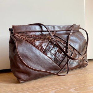 Puede incluir: Bolso de hombro de cuero marrón con un diseño tejido y detalles de piel de serpiente. El bolso tiene una correa larga y forma rectangular. El bolso está hecho de cuero y tiene un estampado de piel de serpiente en el centro.