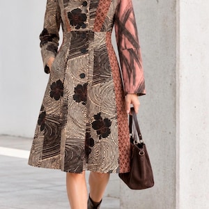 May include: A knee-length coat featuring a patchwork design with brown, black, and tan floral and swirling line patterns. The coat has a collared neckline, long sleeves with pinkish-brown cuffs, a button-front closure, and side pockets.