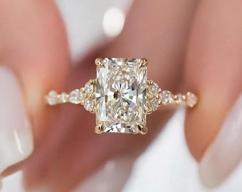 May include: A gold ring featuring a large, rectangular-cut diamond as the centrepiece. The band is also adorned with smaller diamonds. The gold setting highlights the sparkle of the diamonds, creating a luxurious look.