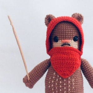 Könnte beinhalten: Ein braunes, gehäkeltes Plüschtier mit einem roten Kapuzenumhang und einem Stock in der Hand. Das Spielzeug ist ein Charakter aus dem Star Wars-Franchise.