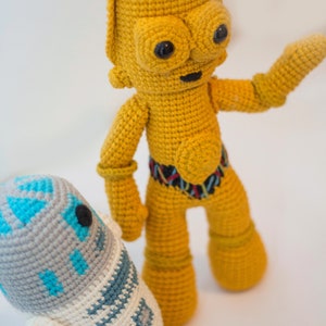 Könnte beinhalten: Ein gehäkelter gelber C-3PO und ein gehäkelter weißer R2-D2. Die Figuren stehen auf einer weißen Oberfläche.