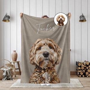 K&ouml;nnte beinhalten: Eine beige Decke mit einem detaillierten Portr&auml;t eines Hundes mit braunem und cremefarbenem Fell. Der Name des Hundes, "Tucker", ist in Schreibschrift &uuml;ber dem Gesicht des Hundes geschrieben. Ein kleineres kreisf&ouml;rmiges Bild des Hundes befindet sich in der oberen rechten Ecke.