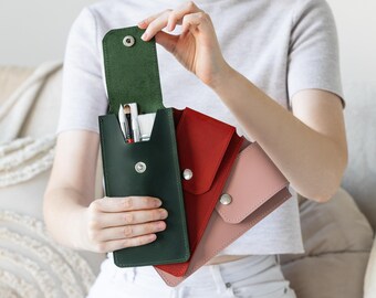 May include: A collection of leather pen or brush cases in various colors. The open, dark green case reveals brushes and pens inside. Other cases are red and pink. Each case has a snap closure.