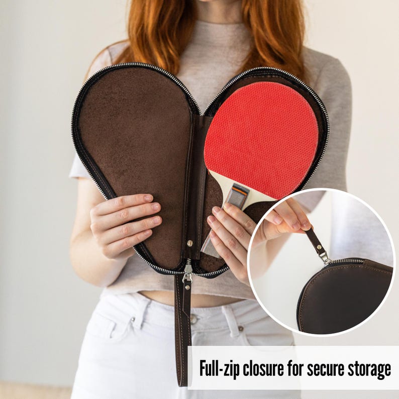 K&ouml;nnte beinhalten: Eine braune Tischtennisschl&auml;ger-Tasche aus Leder mit durchgehendem Rei&szlig;verschluss. Die Tasche ist ge&ouml;ffnet und zeigt einen roten und schwarzen Tischtennisschl&auml;ger. Der Text "Full-zip closure for secure storage" ist sichtbar.