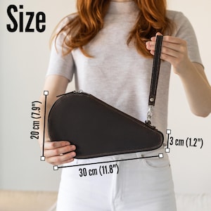 K&ouml;nnte beinhalten: Eine dunkelbraune Leder-Clutch mit Rei&szlig;verschluss und Handschlaufe. Die Clutch ist 30 cm lang, 20 cm hoch und 3 cm dick. Das Wort "Size" wird im Bild angezeigt.