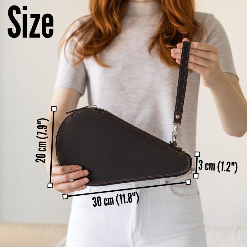 K&ouml;nnte beinhalten: Eine dunkelbraune Leder-Clutch mit Rei&szlig;verschluss und Handschlaufe. Die Clutch ist 30 cm lang, 20 cm hoch und 3 cm dick. Das Wort "Size" wird im Bild angezeigt.