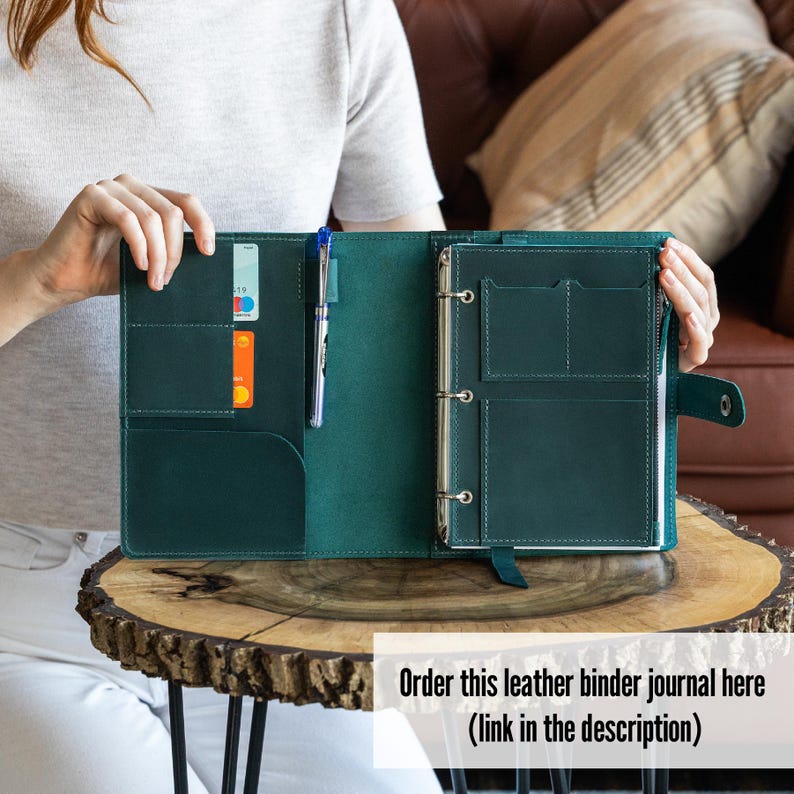 K&ouml;nnte beinhalten: Offenes, teal-farbenes Leder-Ringbuch mit mehreren Taschen, Kartenf&auml;chern und einem Stifthalter. Das Journal ist ge&ouml;ffnet und zeigt das Innere mit Metallringen zum Halten der Seiten. Ein blauer Stift befindet sich im Stifthalter.