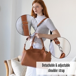 Puede incluir: Un bolso de mano de cuero marr&oacute;n con una correa de hombro desmontable y ajustable. El bolso tiene un asa superior y un bolsillo frontal. La correa est&aacute; sujeta con herrajes met&aacute;licos plateados. El bolso se muestra con una mujer que lleva una camisa gris y pantalones blancos.