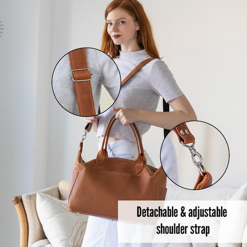 Puede incluir: Un bolso de mano de cuero marr&oacute;n con una correa de hombro desmontable y ajustable. El bolso tiene un asa superior y un bolsillo frontal. La correa est&aacute; sujeta con herrajes met&aacute;licos plateados. El bolso se muestra con una mujer que lleva una camisa gris y pantalones blancos.