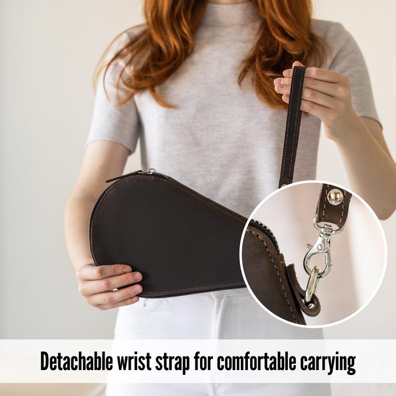 K&ouml;nnte beinhalten: Eine dunkelbraune Ledertasche mit abnehmbarer Handschlaufe. Die Tasche hat einen Rei&szlig;verschluss und einen silberfarbenen Verschluss. Der Text "Detachable wrist strap for comfortable carrying" steht unten.
