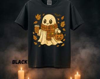 May include: Black t-shirt featuring a cartoon ghost wearing a scarf and holding a coffee cup and a jack-o'-lantern. The ghost is surrounded by autumn leaves and a bat. The word "BLACK" is printed on the shirt.