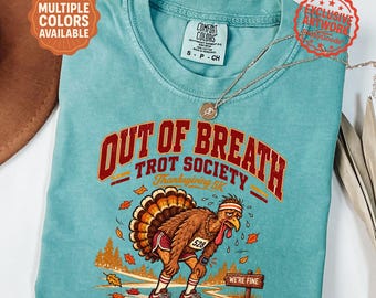 May include: A seafoam green t-shirt featuring a graphic of a tired turkey wearing a headband and running shoes. The text reads OUT OF BREATH TROT SOCIETY Thanksgiving 5K and WE'RE FINE. The turkey wears a race bib with the number 528 and a watch.