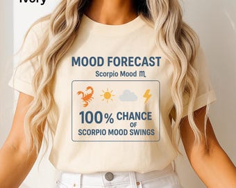 May include: An ivory-coloured t-shirt featuring the words "MOOD FORECAST" and "Scorpio Mood m." A graphic displays a scorpion, sun, cloud, and lightning bolt, with the text "100% CHANCE OF SCORPIO MOOD SWINGS."