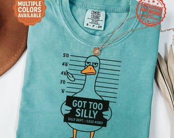 May include: Seafoam green t-shirt featuring a cartoon duck with the text "GOT TOO SILLY" and "SILLY DEPT.-CASE #0001". The shirt has a crew neck and short sleeves. The shirt is labeled "Multiple Colors Available" and "Exclusive Artwork".