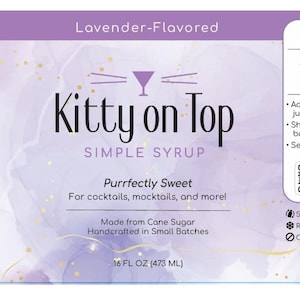 May include: A bottle of "Kitty on Top" lavender-flavored simple syrup, 473 ml, with a cocktail recipe. The label includes nutrition information and the text "Purrfectly Sweet." Made from cane sugar, the syrup is for cocktails and mocktails.