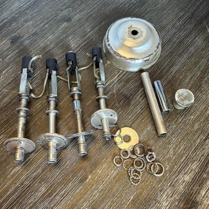 May include: A collection of silver-toned metal lighting components including four vertical socket assemblies with attached wires, a circular canopy cover, a cylindrical tube, a small metal cap, and a cluster of assorted washers and metal rings.