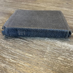 May include: A dark gray, textured hardcover book with a pebbled finish. The spine features the embossed text "HOLY BIBLE" and "MAPS" in a vertical orientation. The book is rectangular with visible wear along the edges and corners of the cover.