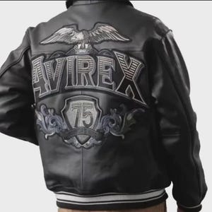 Könnte beinhalten: Schwarze Lederjacke mit dem Wort "AVIREX" und einem großen Adleraufnäher auf dem Rücken. Die Jacke hat einen weiß-schwarzen Streifen am Bund und an den Manschetten. Die Zahl "75" ist ebenfalls auf dem Rücken abgebildet.