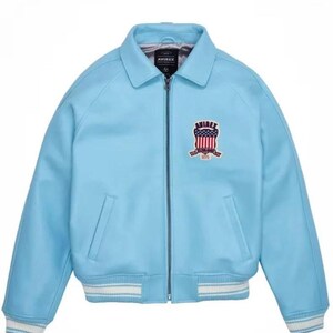 Puede incluir: Chaqueta bomber azul claro con cremallera, dos bolsillos delanteros y cuello. La chaqueta presenta un parche con el texto "AVIREX" y un emblema rojo, blanco y azul. Los pu&ntilde;os y el dobladillo tienen rayas blancas y azul claro.