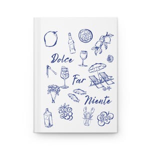 May include: A white journal with a blue pen-and-ink illustration. The design includes lemons, wine glasses, a bottle, and the words "Dolce Far Niente". The journal has a clean, minimalist aesthetic.