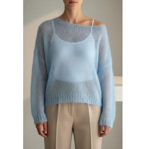 Könnte beinhalten: Hellblauer, durchsichtiger Strickpullover mit langen Ärmeln und einem U-Boot-Ausschnitt. Darunter ist ein hellblaues Camisole zu sehen. Das Model trägt eine beige Hose. Der Pullover ist ein weiches, luftiges Kleidungsstück.