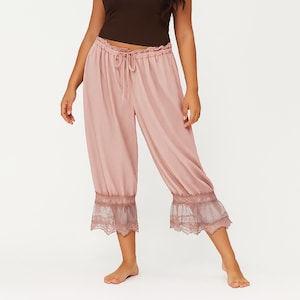 Puede incluir: Pantalones capri rosa empolvado con cintura con cordón y ribete de encaje en el dobladillo. Los pantalones están hechos de una tela ligera y fluida. Los pantalones son de estilo corto.