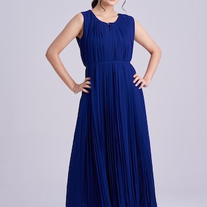 May include: A sleeveless, royal blue pleated maxi dress. The dress features a round neckline, a cinched waist, and a flowing skirt. The model is wearing gold sandals and a gold bracelet. The dress is made of a lightweight fabric.